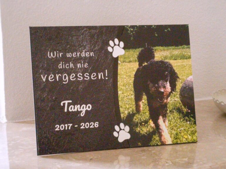 UV-gedrucktes Schild: Schrift Wir werden dich nie vergessen, Name Tango, Jahreszahlen 2017 bis 2026, zwei Pfoten und ein Foto eines schwarzen Hundes.